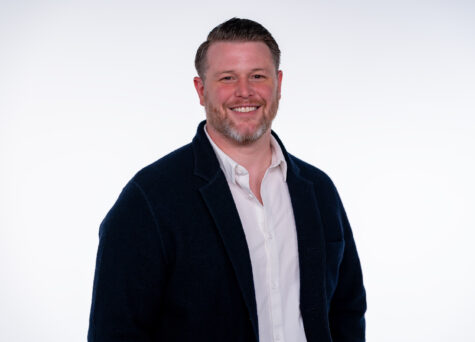 Portrait of Dan Law smiling wearing a navy blazer and white shirt, against a plain white background.