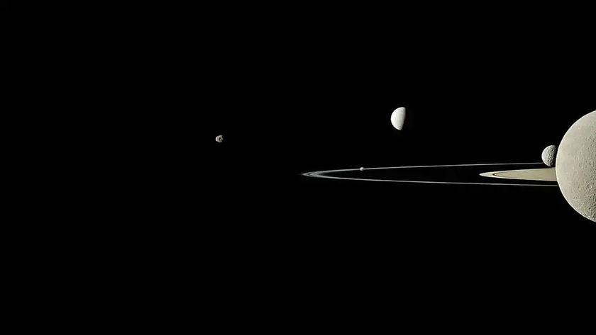 A black background with Saturn toward the right, half off screen. Above and below its rings, which go toward the left, there are orbs of different sizes.